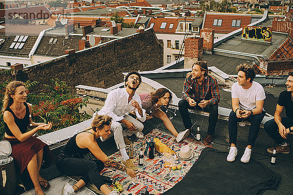 Fröhliche männliche und weibliche Freunde genießen auf der Terrasse während einer Dachparty