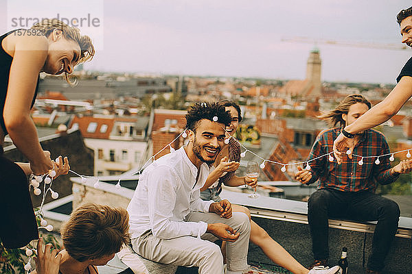 Verspielte Freunde genießen mit Schnurlicht auf der Terrasse während der Dachparty