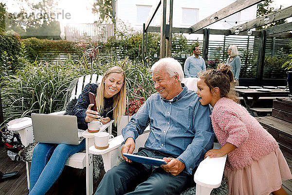 Lächelnde Familie nutzt digitale Technologie  während sie am Wochenende im Hinterhof sitzt