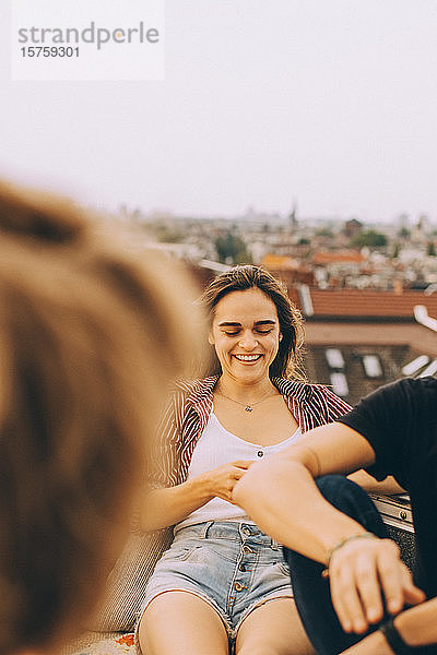 Lächelnde junge Frau amüsiert sich mit Freunden auf der Terrasse bei einer Dachfeier