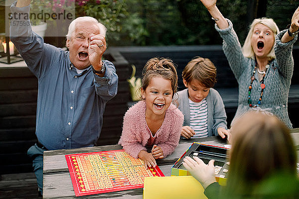 Lächelnde  fröhliche Familie spielt Brettspiel  während sie im Hinterhof am Tisch sitzt