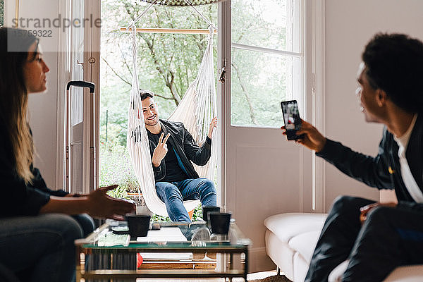 Mann fotografiert Freund mit Smartphone  während er zu Hause in der Schaukel sitzt
