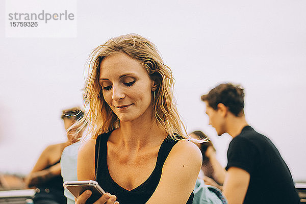 Lächelnde Frau benutzt Mobiltelefon während einer Dachfeier
