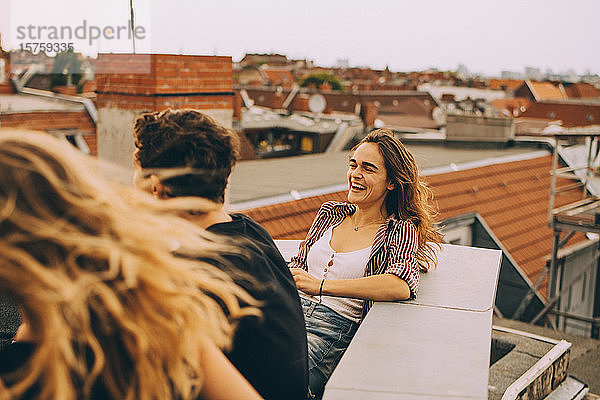 Fröhliche junge Frau genießt Dachfeier mit Freunden auf der Terrasse der Stadt