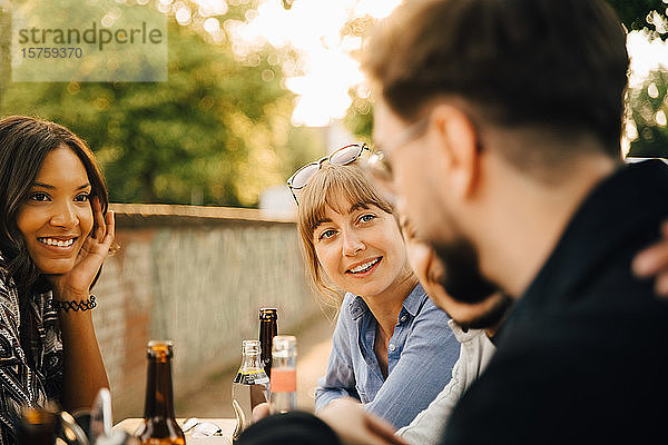 Lächelnde Frauen sitzen neben männlichen Freunden auf Gartenparty