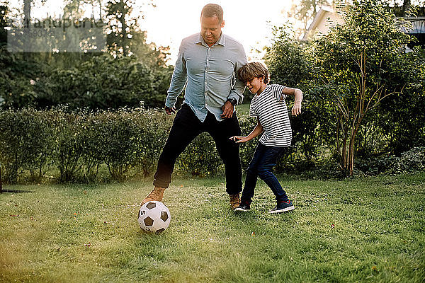 Volle Länge von Vater und Sohn beim Fußballspielen im Hinterhof während der Wochenendaktivitäten