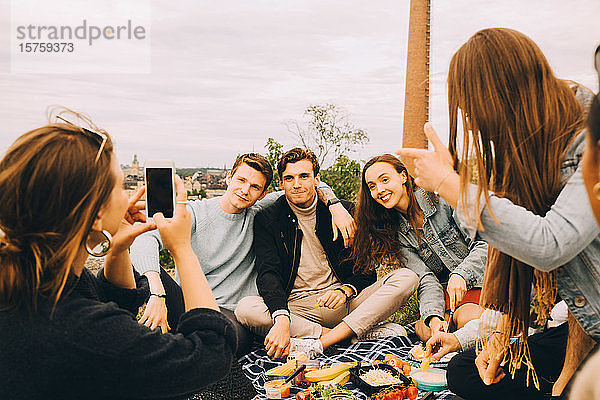 Frau fotografiert Freunde beim gemeinsamen Picknick gegen den Himmel