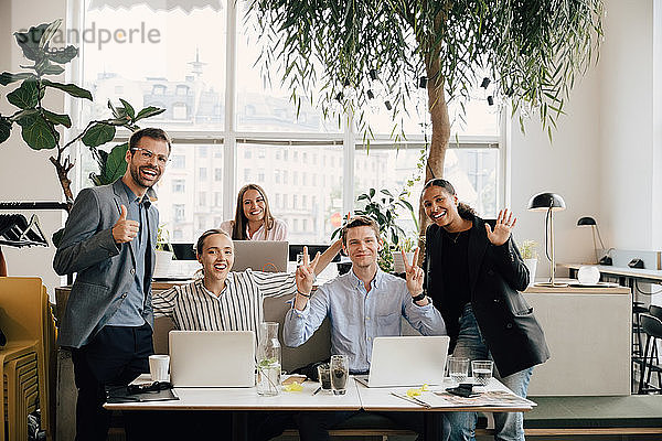 Porträt von lächelnden Kollegen mit Laptops  die am Schreibtisch im Coworking Space gestikulieren