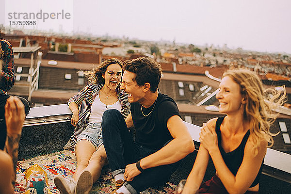Fröhliche männliche und weibliche Freunde genießen auf der Terrasse während einer Dachparty