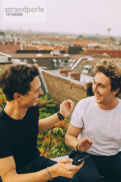 Mann zeigt einem Freund sein Handy und trinkt während der Party auf der Terrasse