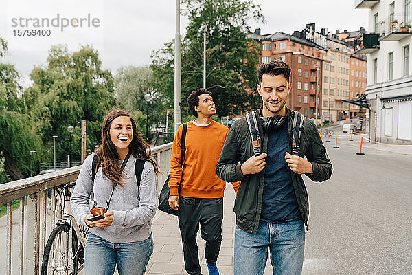 Lächelnde Freunde gehen auf der Straße  während sie im Urlaub die Stadt erkunden