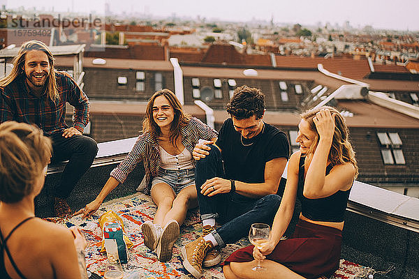 Männliche und weibliche Freunde unterhalten sich  während sie während der Party auf der Terrasse zusammen sitzen