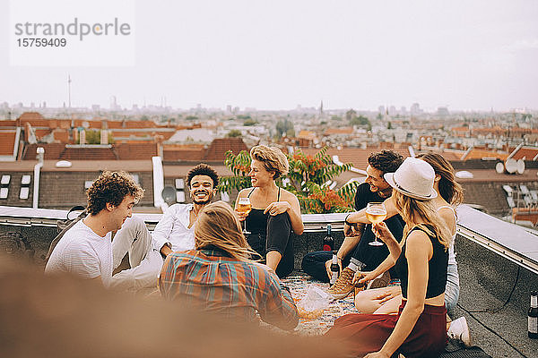 Freunde genießen Bier  während sie bei einer Dachfeier auf der Terrasse zusammen sitzen