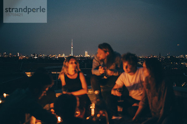 Freunde genießen in der Dämmerung auf der Terrasse gegen das Stadtbild