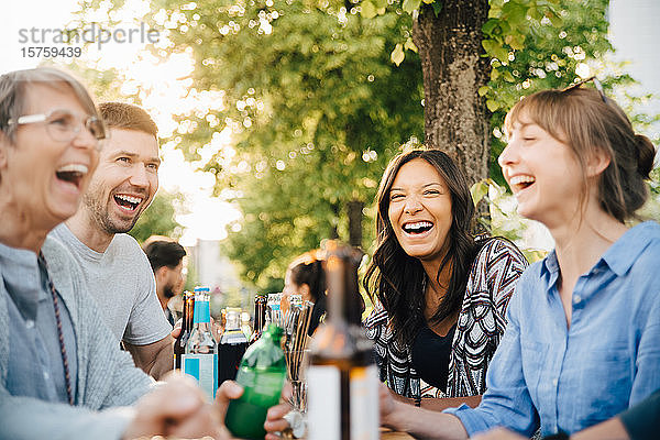 Lachende Freunde und Freundinnen beim Sitzen mit Getränken im Biergarten