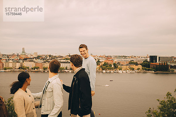 Freunde schauen auf lächelnden Mann  der in der Stadt am See steht