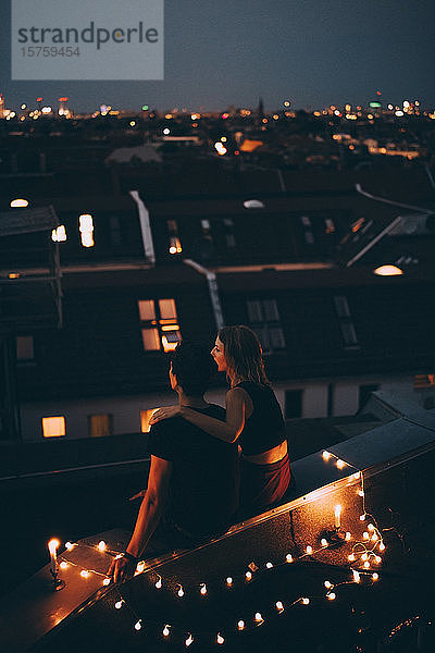 Hochwinkelansicht eines Paares  das in der Abenddämmerung auf einer beleuchteten Terrasse in der Stadt sitzt