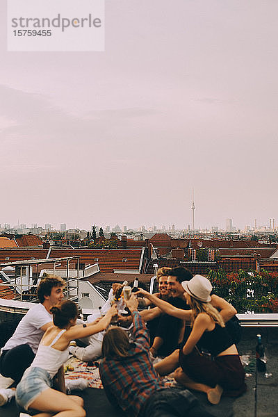 Männliche und weibliche Freunde stoßen auf Bier an  während sie sich auf einer Terrasse in der Stadt entspannen