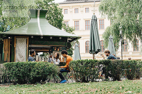 Lächelnde Freunde sitzen am Konzessionsstand bei Pflanzen in der Stadt