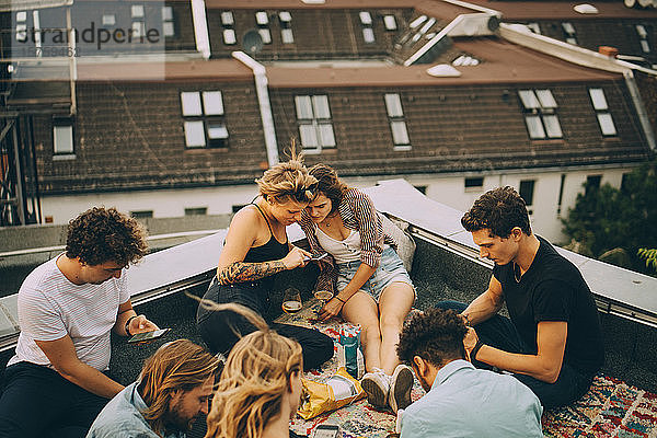 Freunde und Freundinnen benutzen Smartphones  während sie während der Party auf der Terrasse sitzen