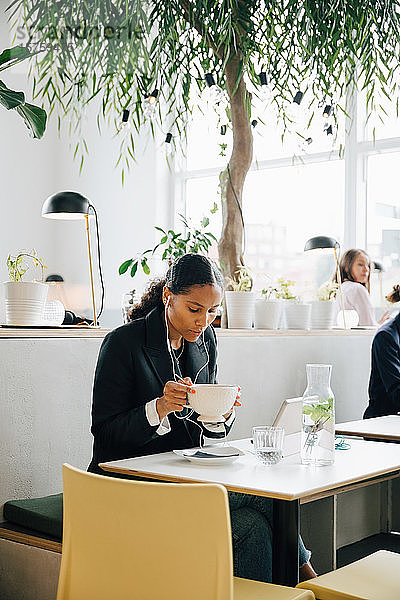 Geschäftsfrau trägt Kopfhörer und isst Suppe im Bürocafé