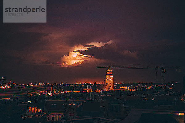 Beleuchteter Uhrturm inmitten des Stadtbildes gegen den Himmel in der Dämmerung