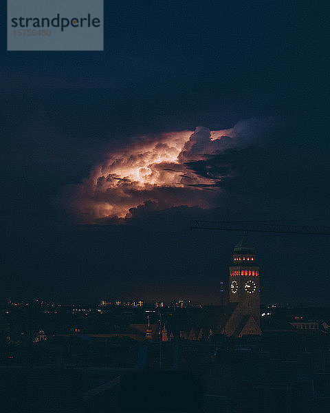 Beleuchteter Uhrturm inmitten des Stadtbildes gegen den nächtlichen Himmel
