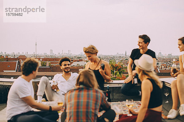 Männliche und weibliche Freunde amüsieren sich auf der Terrasse bei einer Dachfeier