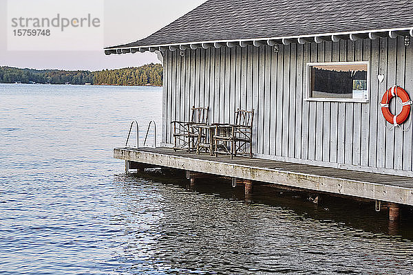 Eine über dem Wasser eines Sees gebaute Hütte am Wasser  Stühle aus Baumzweigen auf der Veranda