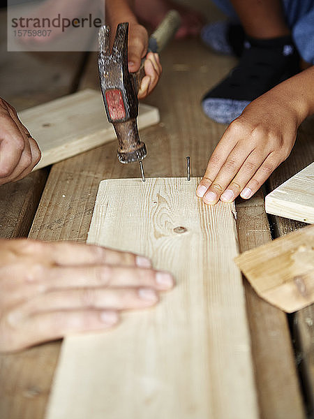 Zimmermann und zwei weitere Personen schlagen Nägel in Holzbohlen ein