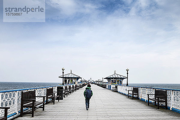 Junge  der an einem Pier am Meer spazieren geht.