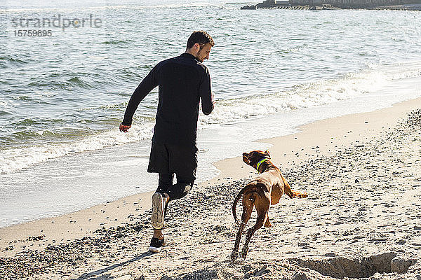 Mann joggt mit Hund am Strand