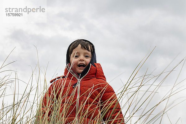 Junge in roter Kugelfischjacke hinter langem Gras