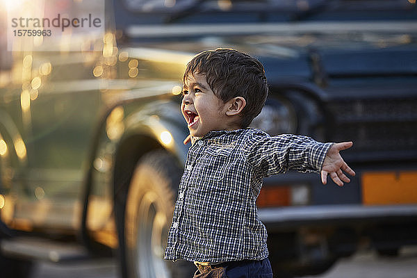 Aufgeregtes Kleinkind mit offenen Armen neben einem großen Fahrzeug stehend