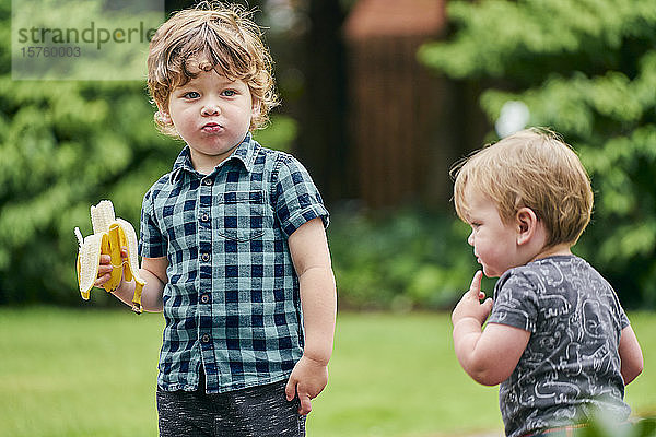 Kleinkinder erkunden und essen Banane im Park