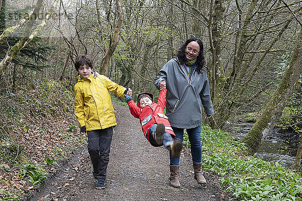 Mutter und Söhne gehen gemeinsam an einem nebligen Regentag im Wald spazieren.
