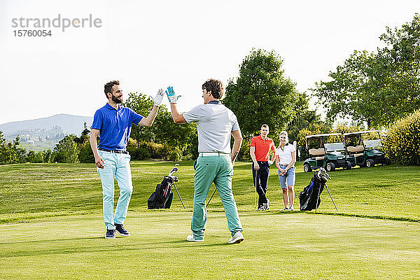 Freunde geben High Five auf dem Golfplatz  ein Paar schaut im Hintergrund zu