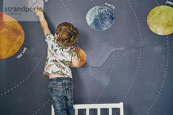 Kleinkind spielt mit Spielzeug an Wand mit Wandbild des Sonnensystems