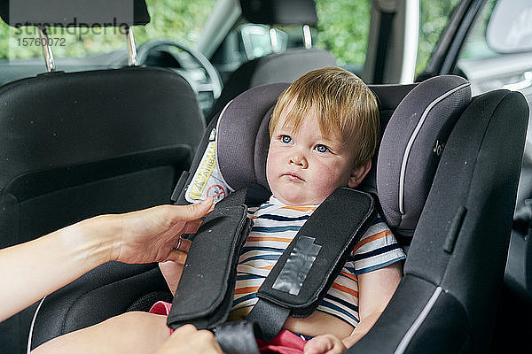 Kleinkind wird auf dem Rücksitz eines Familienautos in einen Kinderautositz angeschnallt.