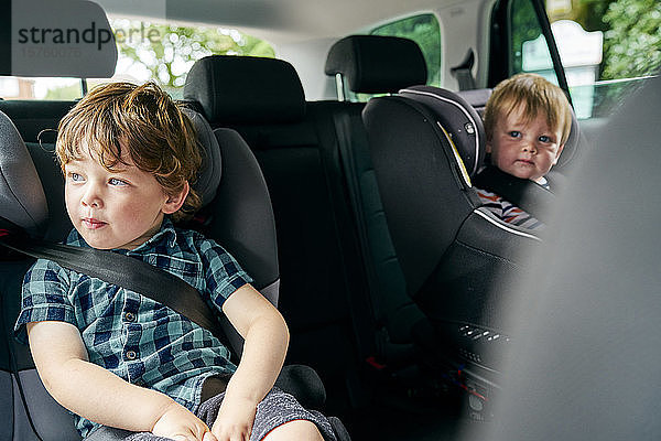 Brüder  die auf Kindersitzen auf dem Rücksitz eines Familienautos angeschnallt sind.