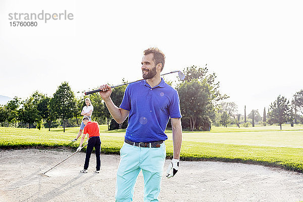 Mann mit Golfschläger auf dem Golfplatz  Freunde spielen Golf im Hintergrund