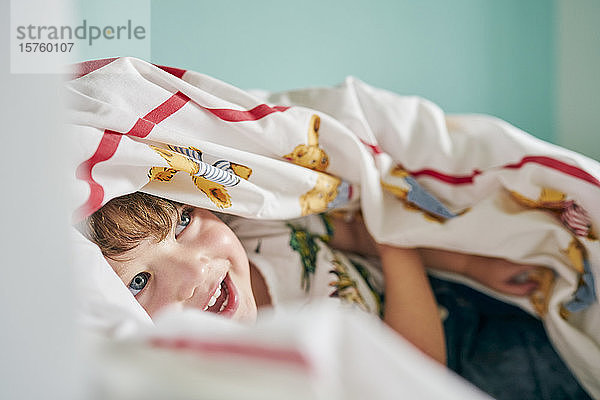 Kleinkind versteckt sich unter einer Decke im Zimmer