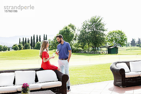 Paar mit Weingläsern unterhält sich neben dem Sofa auf dem Golfplatz