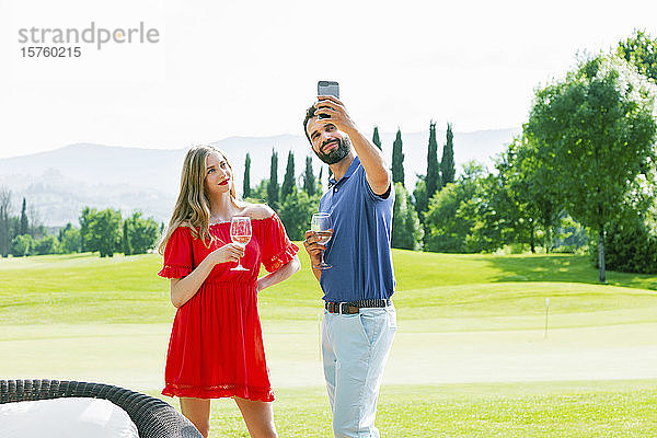 Paar mit Weingläsern beim Selfie auf dem Golfplatz