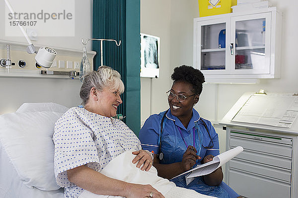 Weibliche Krankenschwester im Gespräch mit einem älteren Patienten im Krankenhauszimmer