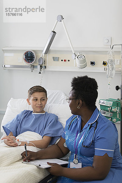 Krankenschwester mit Klemmbrett im Gespräch mit einem jungen Patienten im Krankenhauszimmer