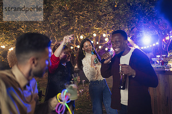 Freunde tanzen und singen Karaoke auf einer Gartenparty
