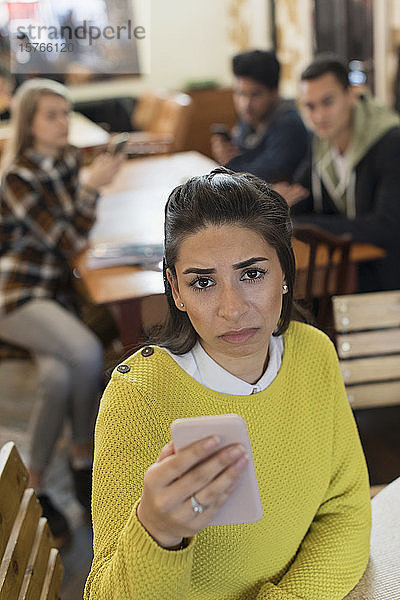 Porträt einer verärgerten jungen Frau mit Smartphone in einem Café