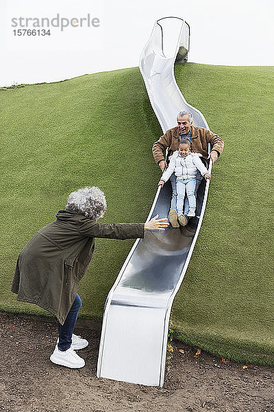Großeltern mit Enkelin auf Spielplatzrutsche