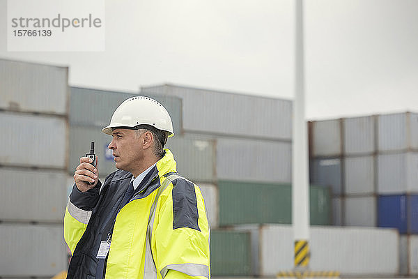 Dockmanager mit Walkie-Talkie zwischen Frachtcontainern auf einer Werft